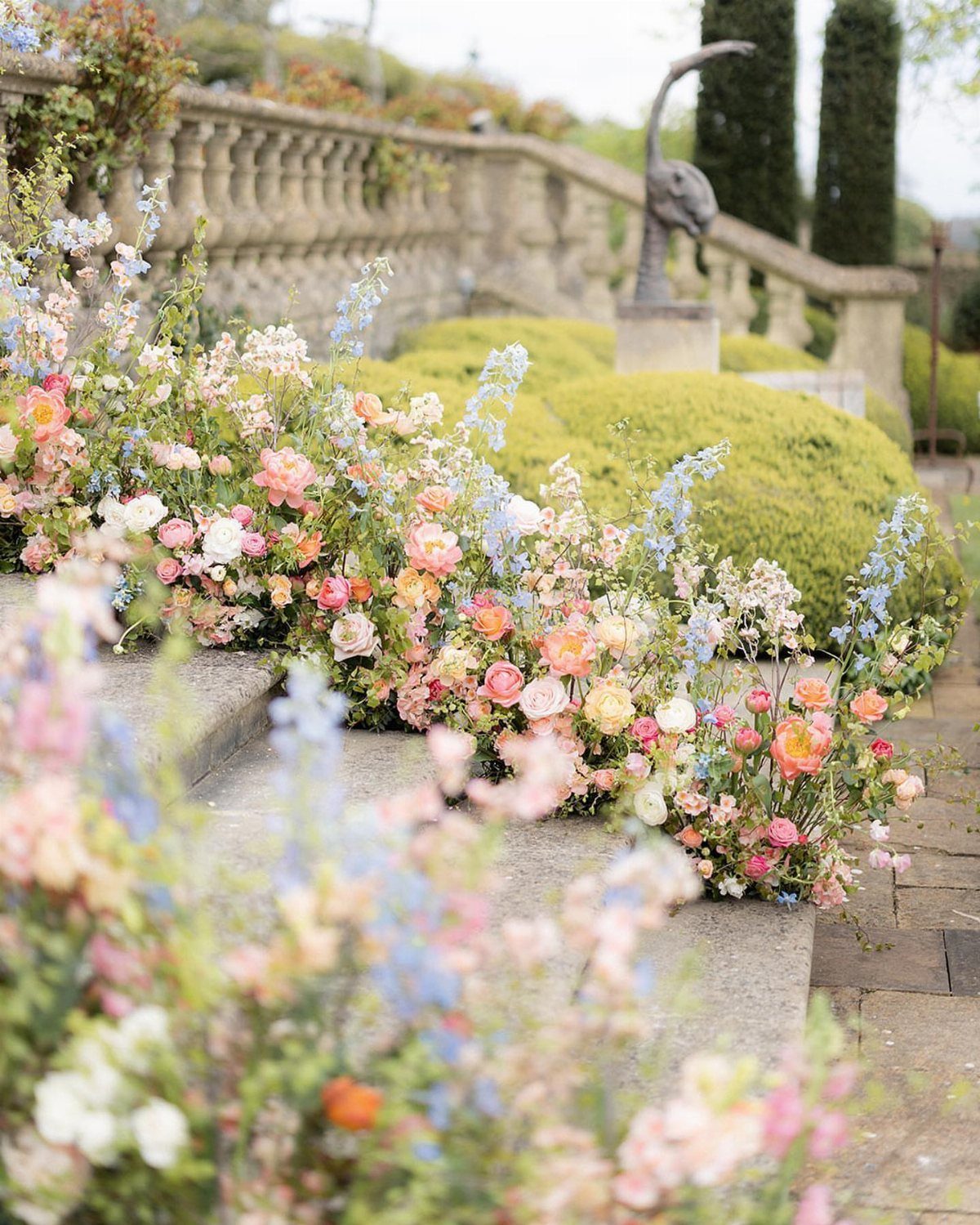 20 Spring Wedding Theme Ideas for 2026 16 Pastel colored flowers growing along stone steps and a garden balustrade outdoors.