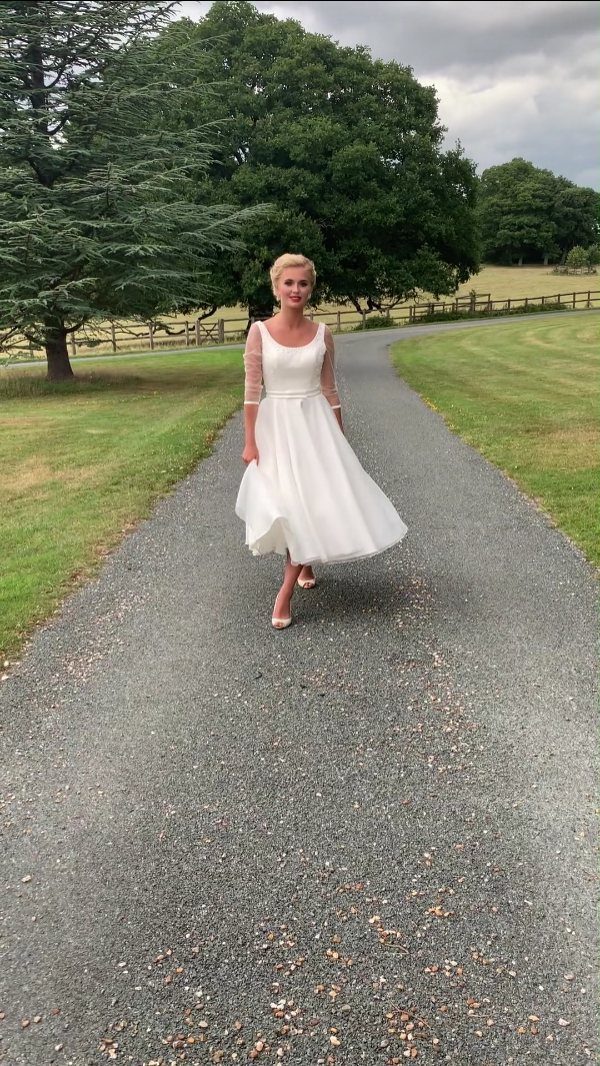 20 Spring Wedding Theme Ideas for 2026 19 A woman in a white tea-length lace wedding dress walking on a gravel path.