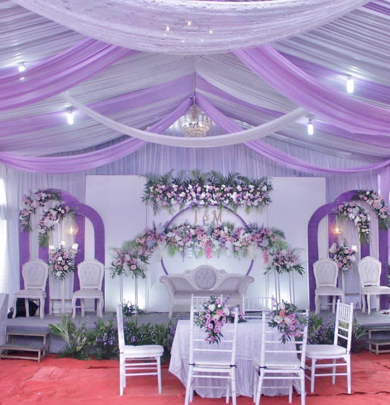 20 Spring Wedding Theme Ideas for 2026 5 Wedding reception decor with purple draped fabric, floral arches, and white furniture.