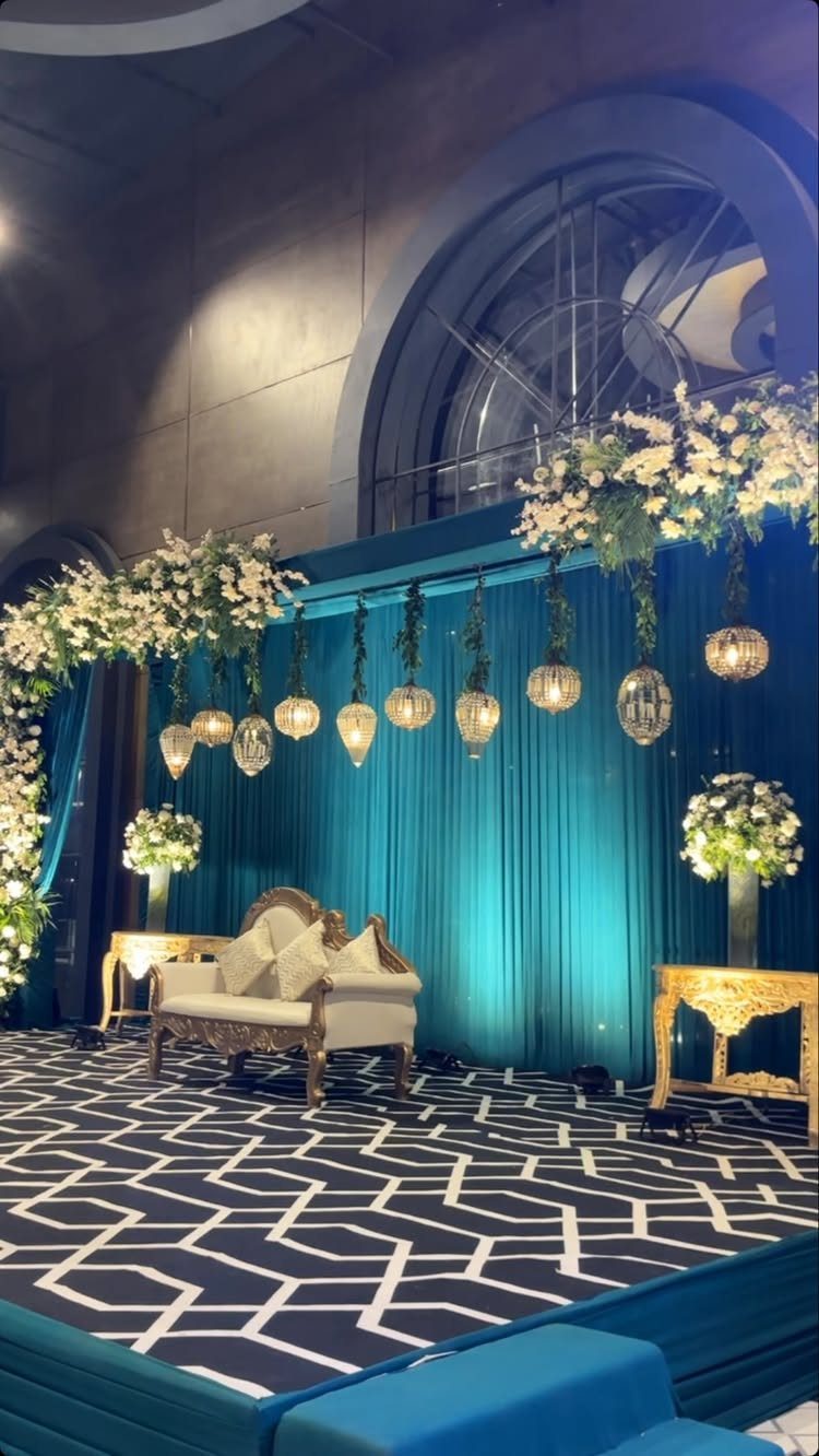 10 Wedding Theme Teal Ideas for Color, Decor and Attire 8 An ornate wedding stage with teal curtains, white flowers, hanging lanterns, and a white loveseat.
