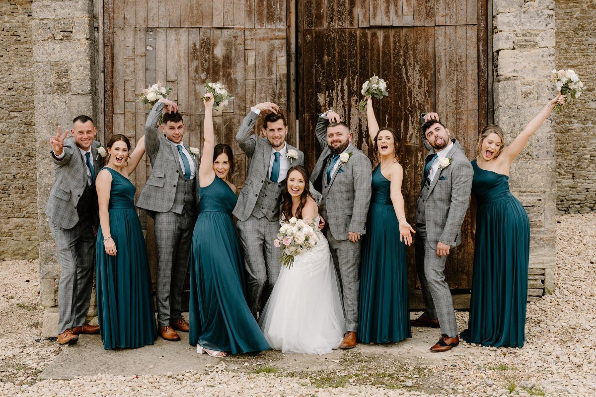 10 Wedding Theme Teal Ideas for Color, Decor and Attire 1 Wedding party posing in teal dresses and grey suits in front of wooden doors.