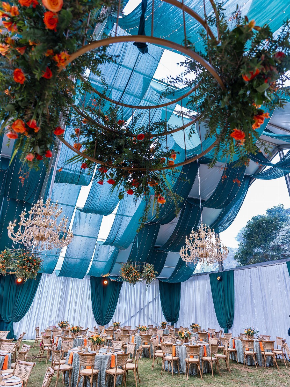 10 Wedding Theme Teal Ideas for Color, Decor and Attire 3 Wedding reception setup featuring teal fabric draping and orange floral arrangements hanging from a canopy.