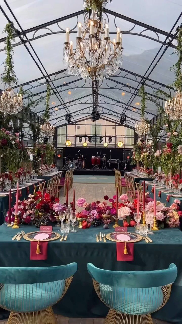 10 Wedding Theme Teal Ideas for Color, Decor and Attire 9 A long wedding reception table decorated with teal linens, pink floral arrangements, and gold accents under a glass marquee.