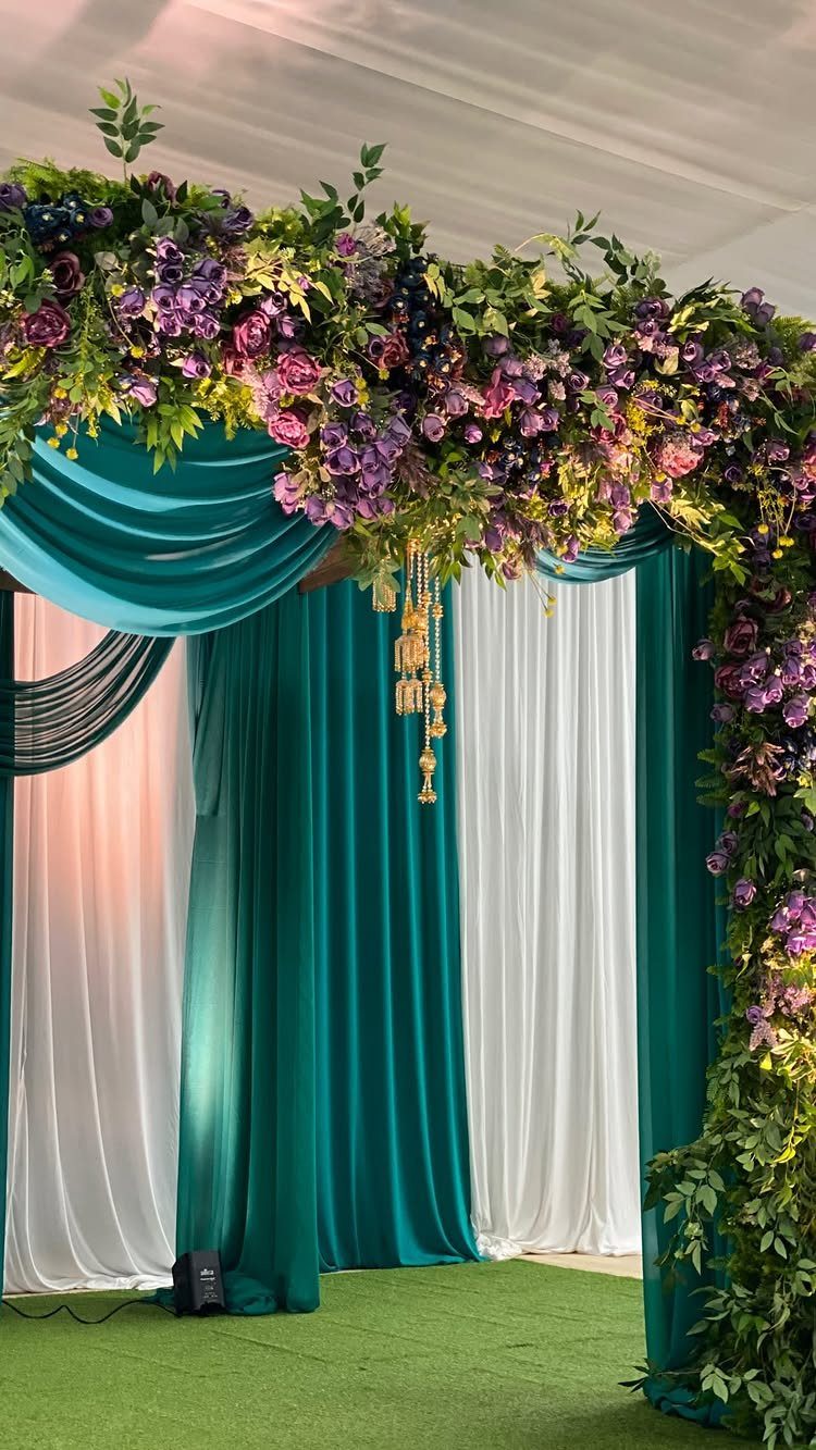 10 Wedding Theme Teal Ideas for Color, Decor and Attire 4 Teal and white fabric drapes decorated with a lush arch of green leaves and purple flowers.
