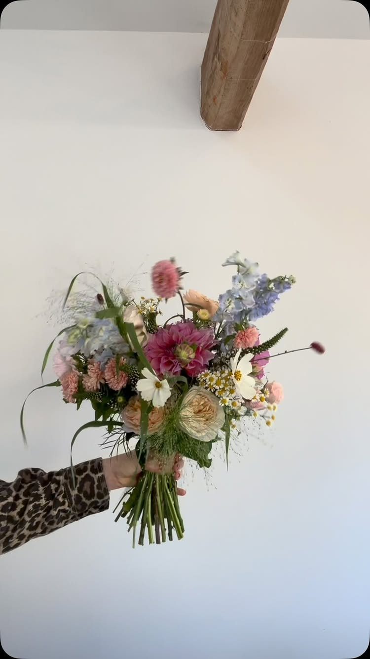 A hand holding a colorful bouquet of wildflowers including pink, white, and blue blossoms.