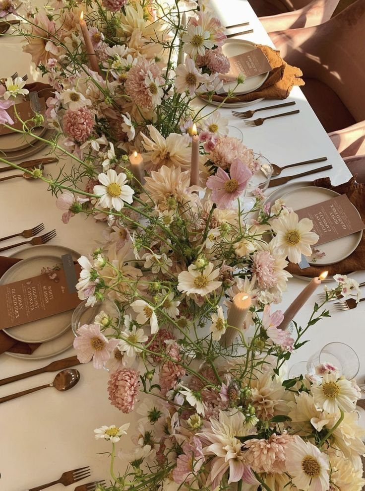 Wildflower floral runner with taper candles decorating a rustic wedding table setting with plates and menus.