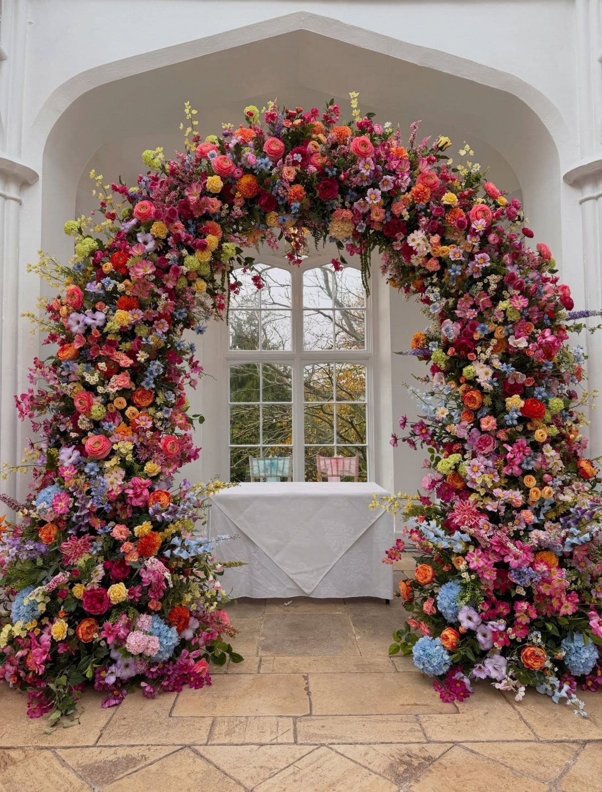 A vibrant, multicolored wildflower arch framing a window and a white table in a bright room.