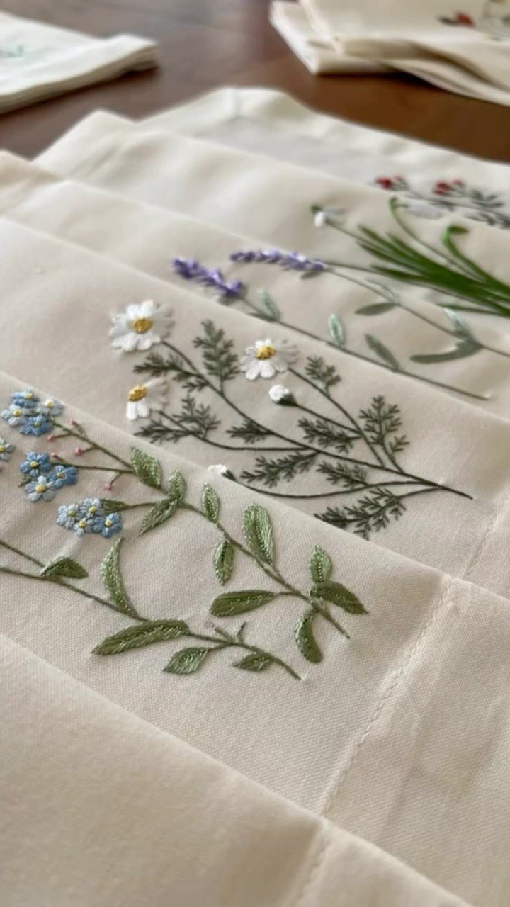 Embroidered white linen napkins with colorful wildflower patterns laid on a wooden table.