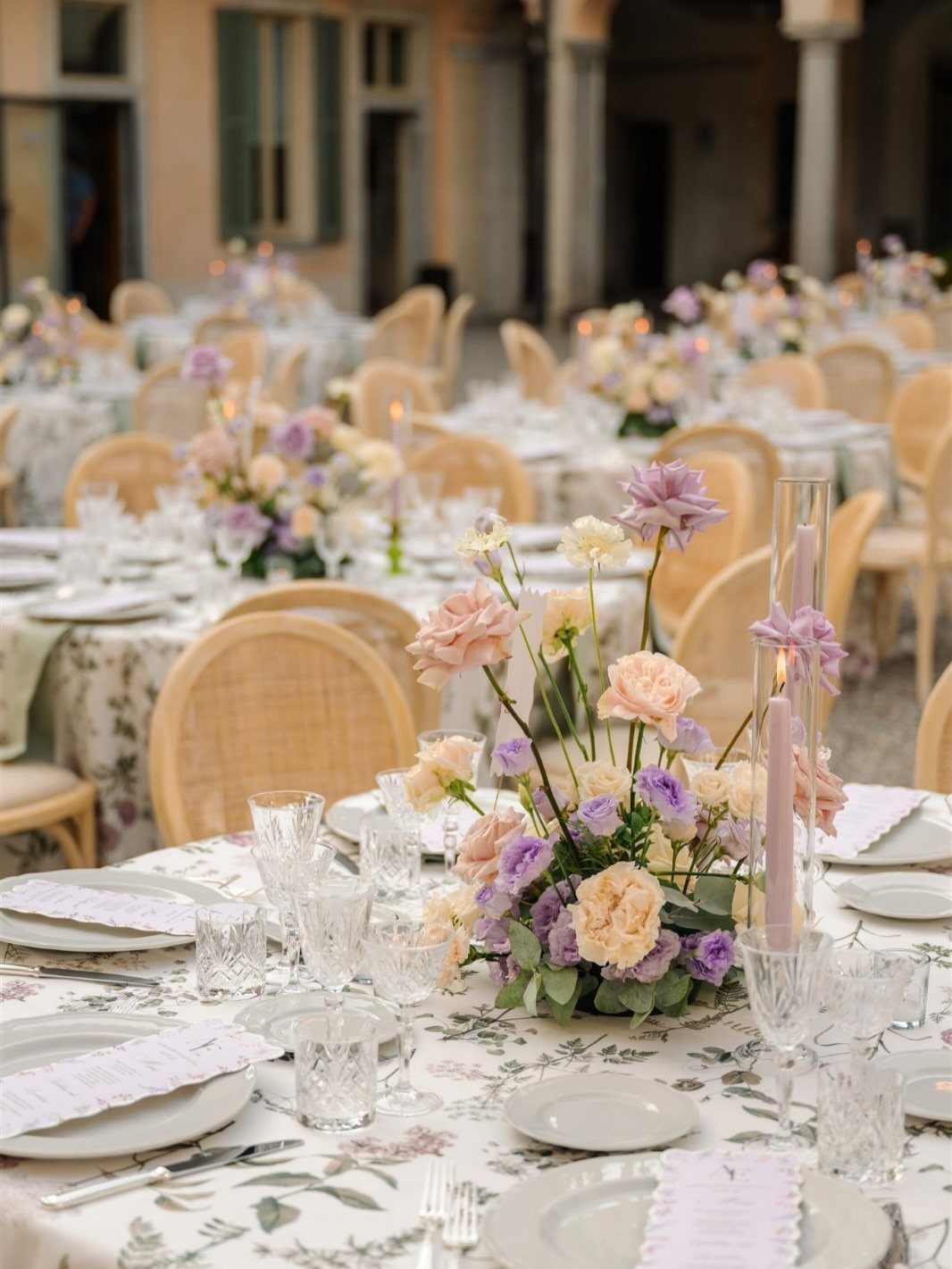 A wedding table set with floral patterned tablecloth, wildflowers, and elegant glassware outdoors.
