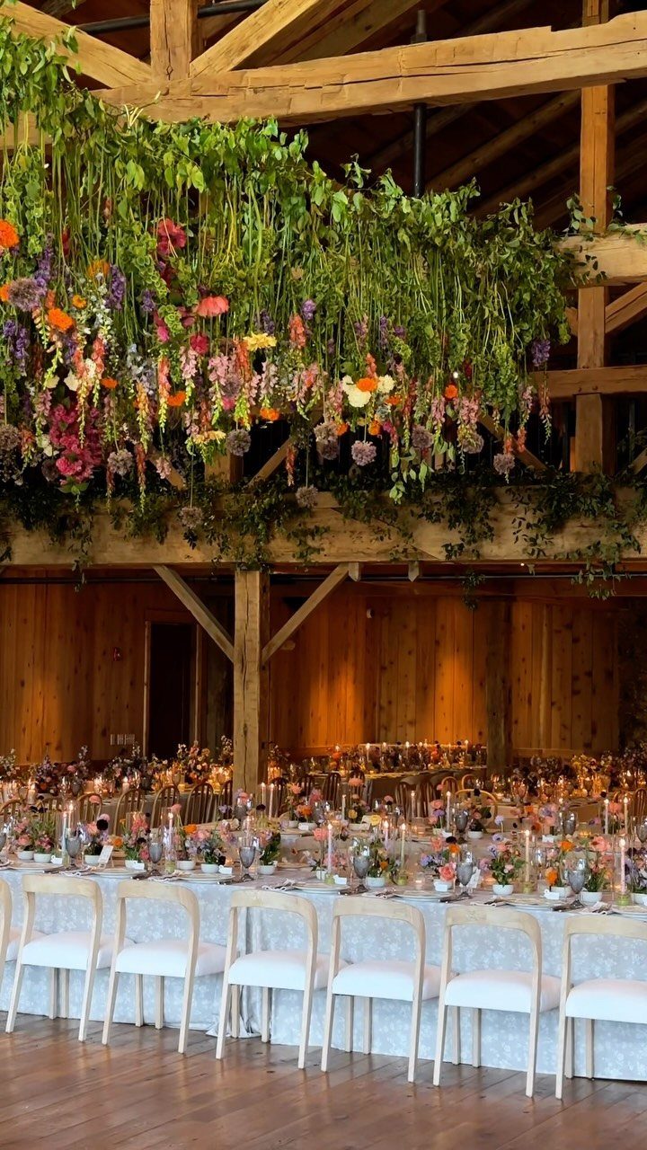 Wildflower arrangements on a long wedding table under a hanging floral installation in a wooden barn.