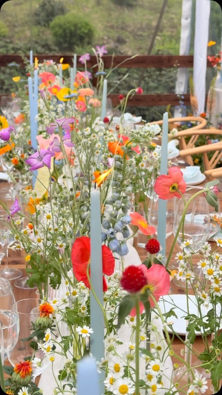 Wildflowers and light blue taper candles decorating a long wooden wedding reception table.